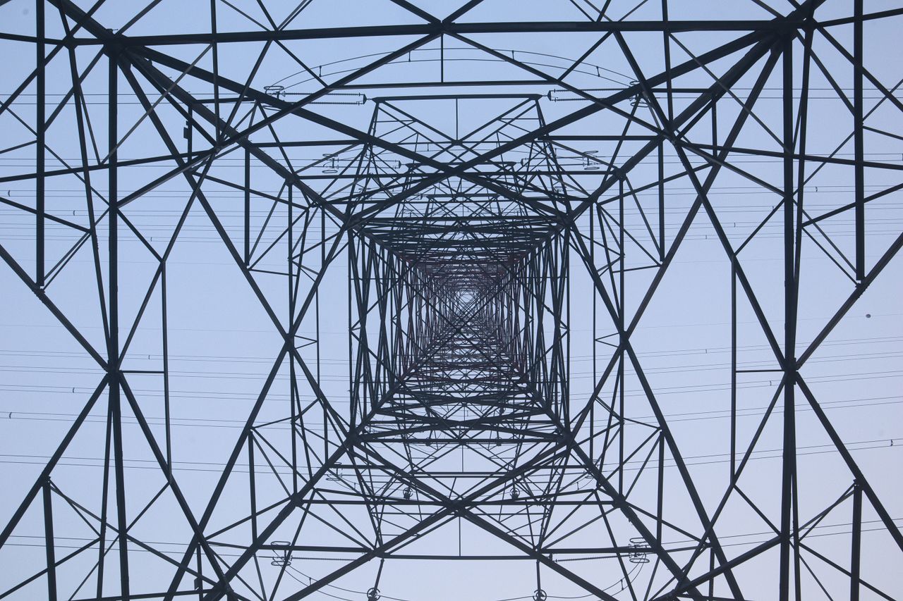 Low angle symmetrical view inside a metal transmission tower against a clear blue sky.