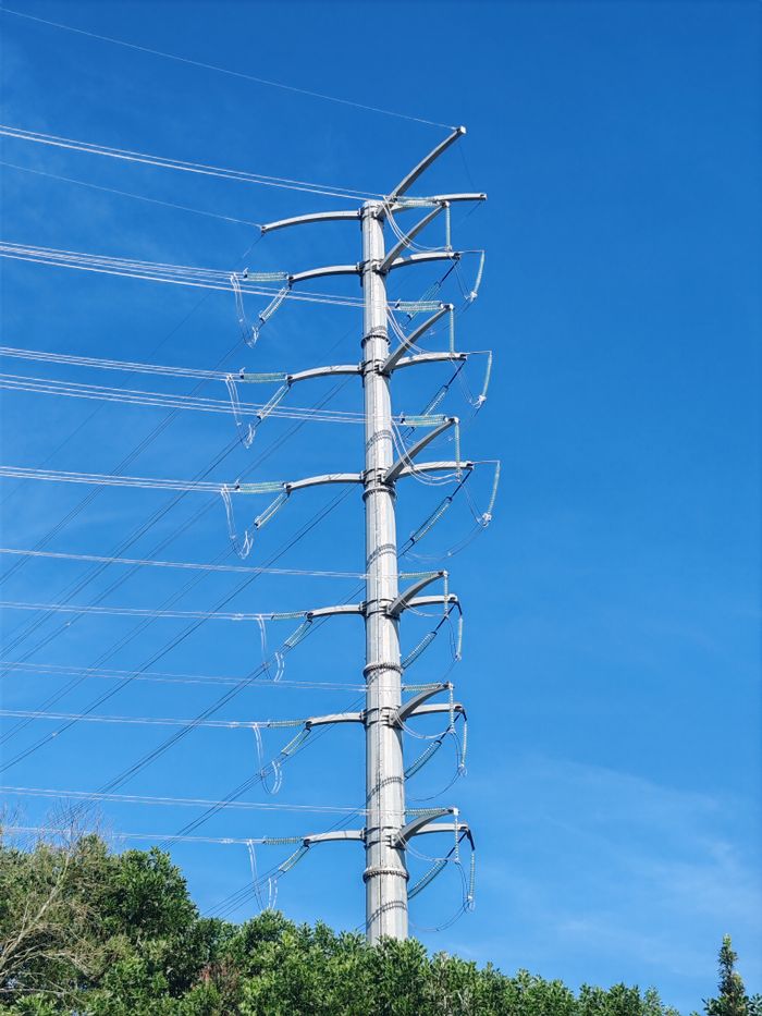 Vertical shot of a steel power transmission tower with cables under a clear blue sky, symbolizing electricity and energy.